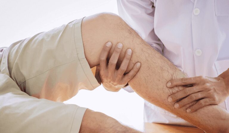 Lekarz bada zgięte kolano pacjenta, wskazując na ocenę fizyczną, prawdopodobnie pod kątem bólu stawu lub diagnozy urazu.