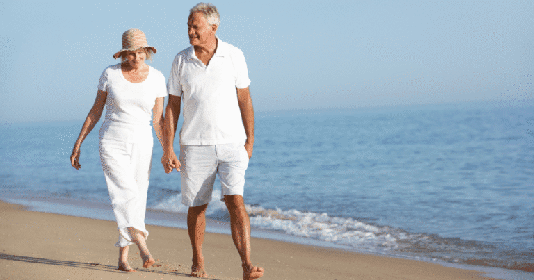 Older couple walking along a beach in Tampa, highlighting an active lifestyle after minimally invasive vein treatment