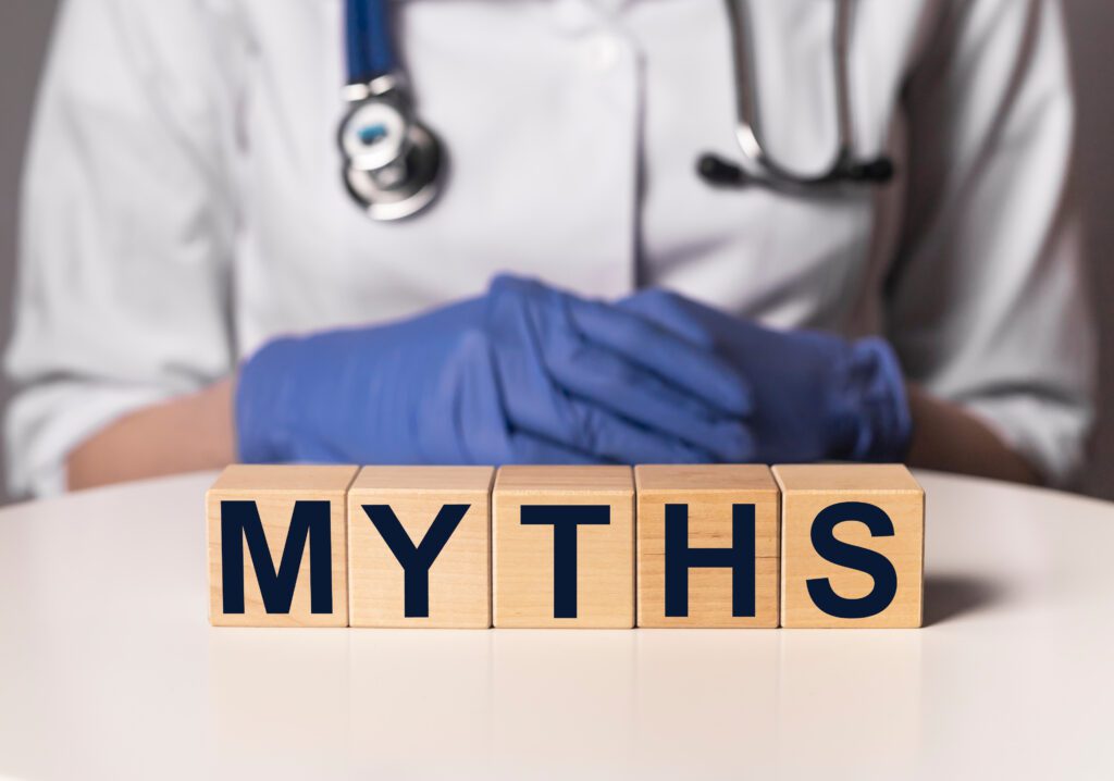A doctor with gloved hands sitting behind wooden blocks that spell out the word myths