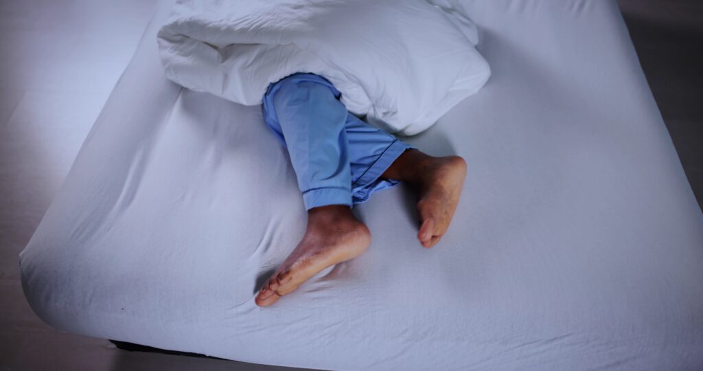 A person lying in bed at night with their lower legs exposed due to nighttime leg pain