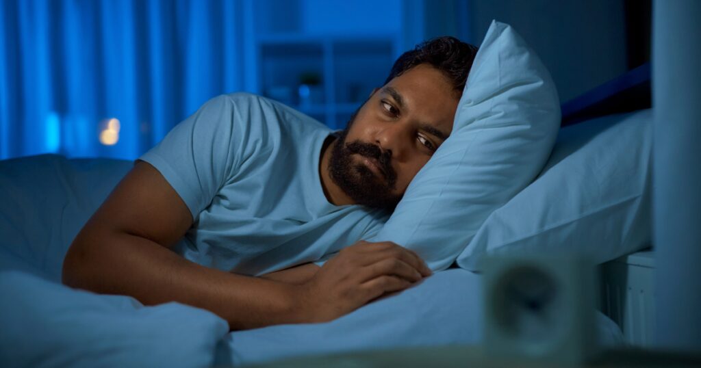 Man laying in bed experiencing the symptom of frequent urination