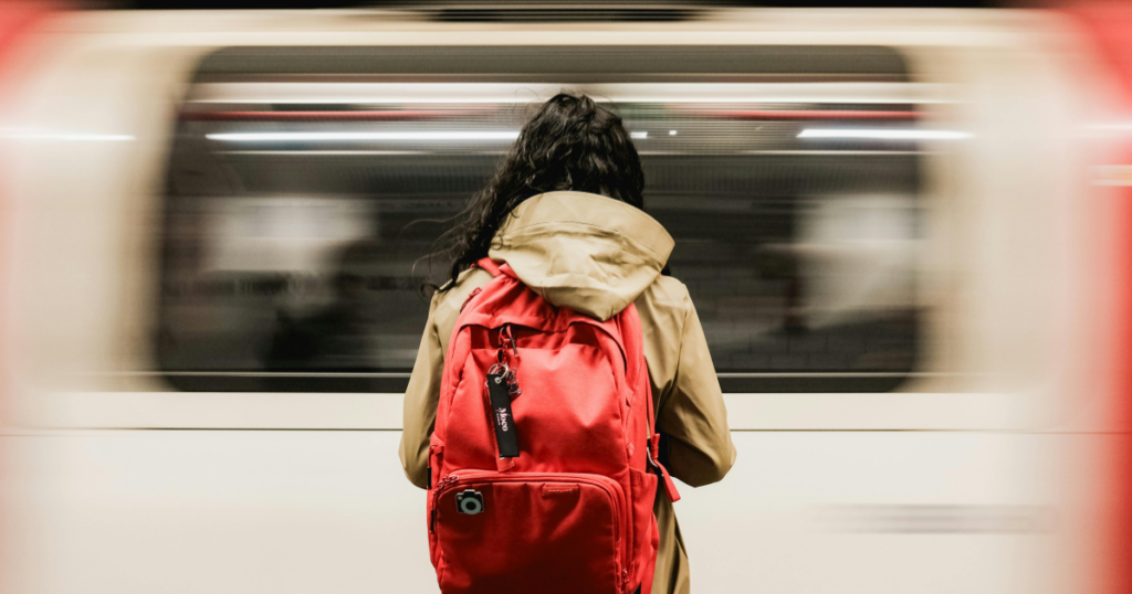 Woman standing on subway platform in front of L train, highlighting urban life and commuting stress related to hemorrhoid symptoms
