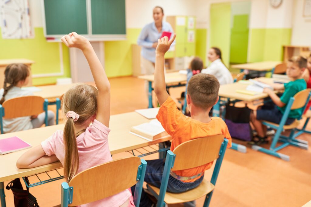 Children raising their hands in an elementary classroom during a lesson.
