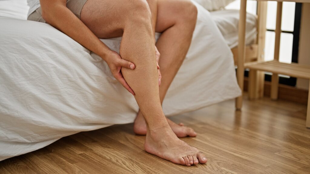 A man holding his painful, heavy leg before standing up from bed.