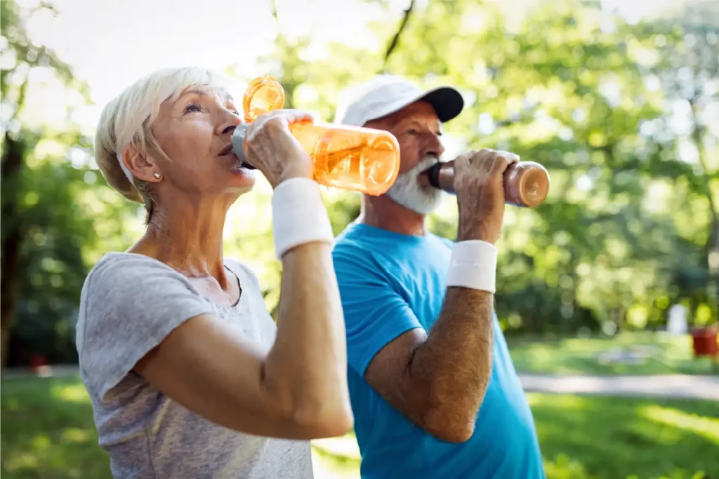 A senior man and woman stand side by side while drinking water after a workout in Duluth, GA