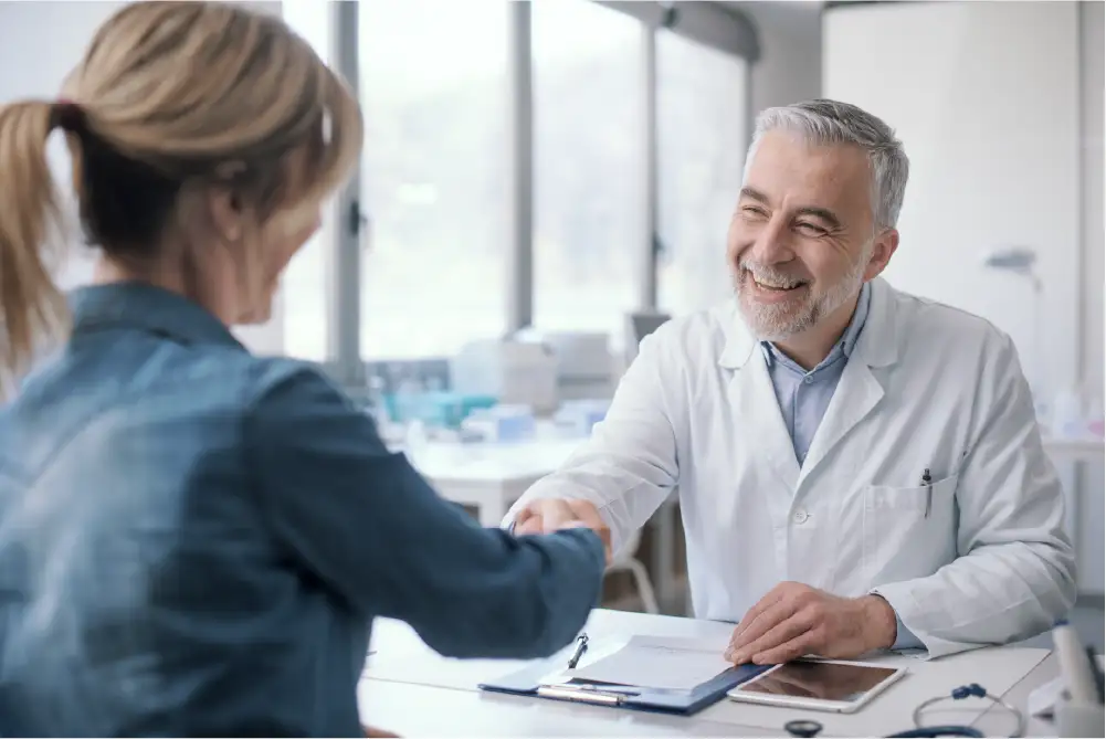 A female patient is shaking hands with a vein specialist with a smile on his face.