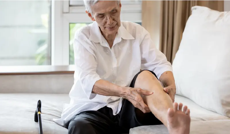 An older man sits on the edge of his bed rubbing on a cramping calf muscle