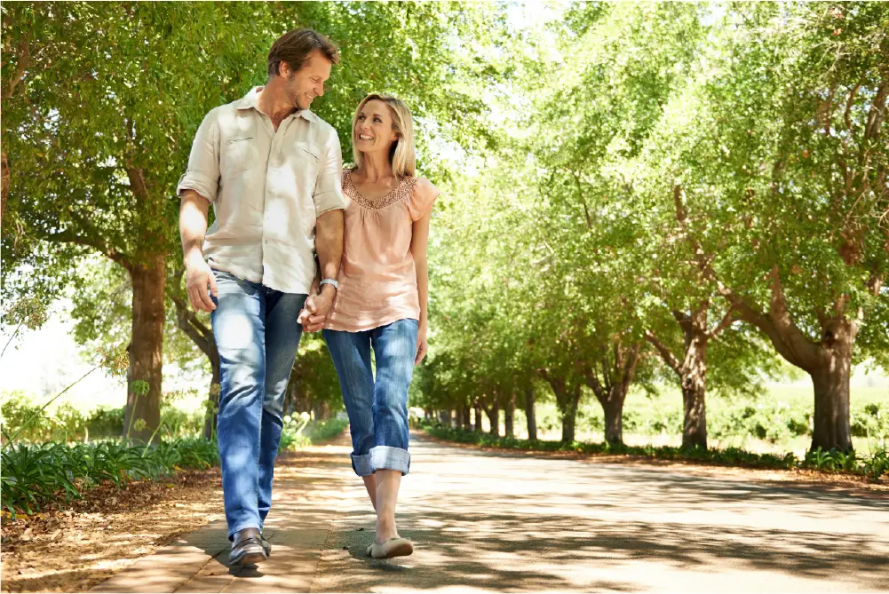 A middle-aged man and woman enjoy strolling in the park together after receiving vein care at a local vein clinic