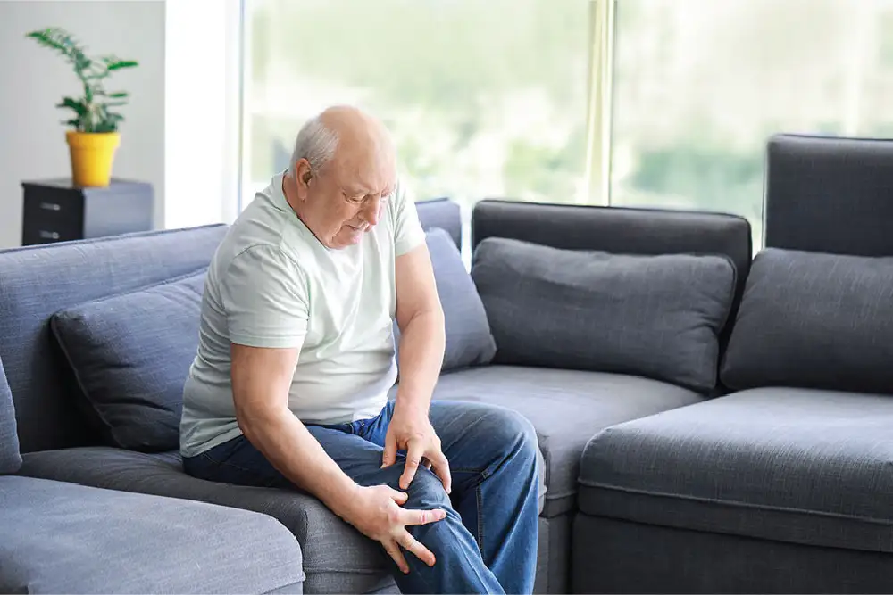 A man sitting on his couch and grasping at his leg in pain