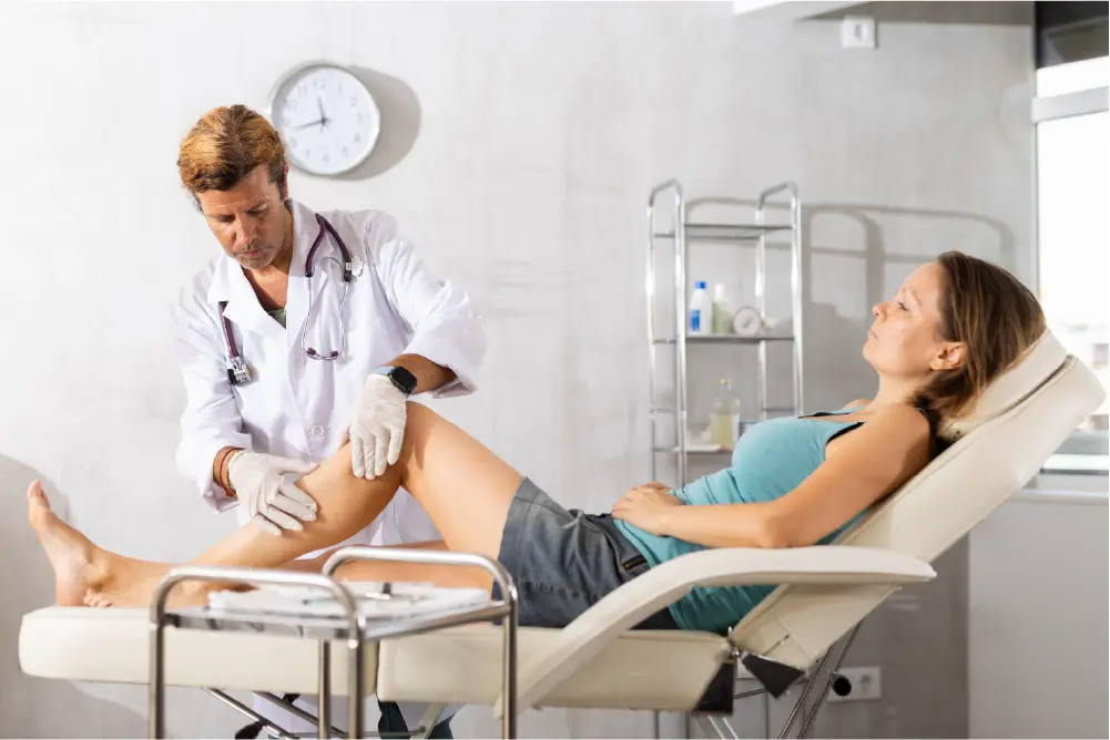 A vein doctor is examining a female patient's lower leg while she lies on the exam table.
